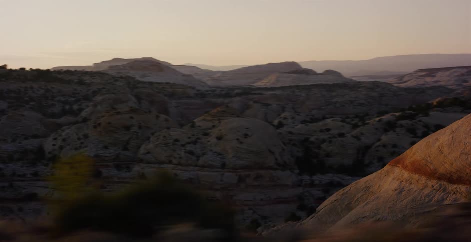 The camera pans across a vast desert canyon landscape, with layered rock formations glowing in the warm light of the setting sun