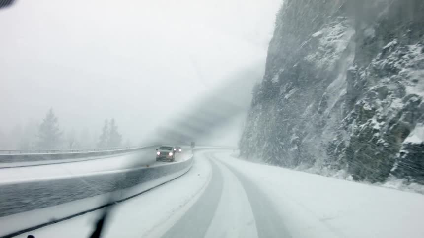 Cars traveling down a snow covered highway in a snowstorm