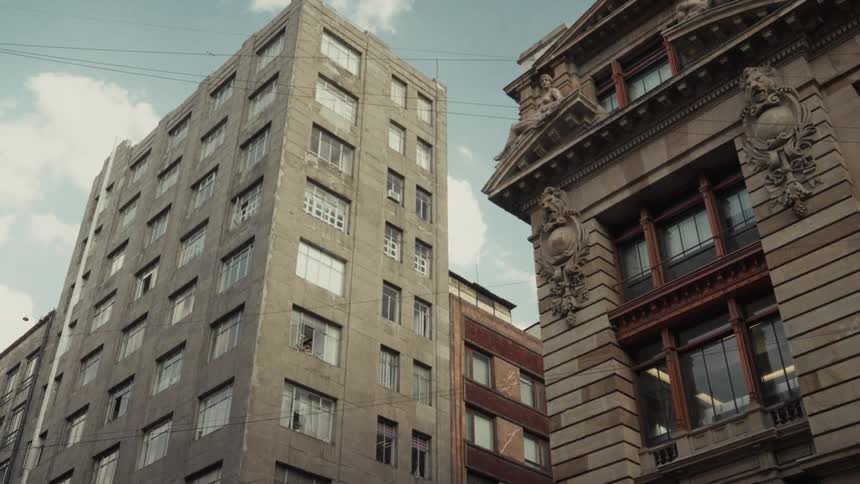 A static low-angle view showcases two contrasting buildings, one modern and one classical, in an urban setting