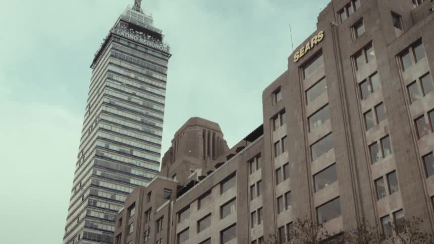 A low-angle tilt-up shot of the Torre Latinoamericana skyscraper and a Sears building in downtown Mexico City on a cloudy day