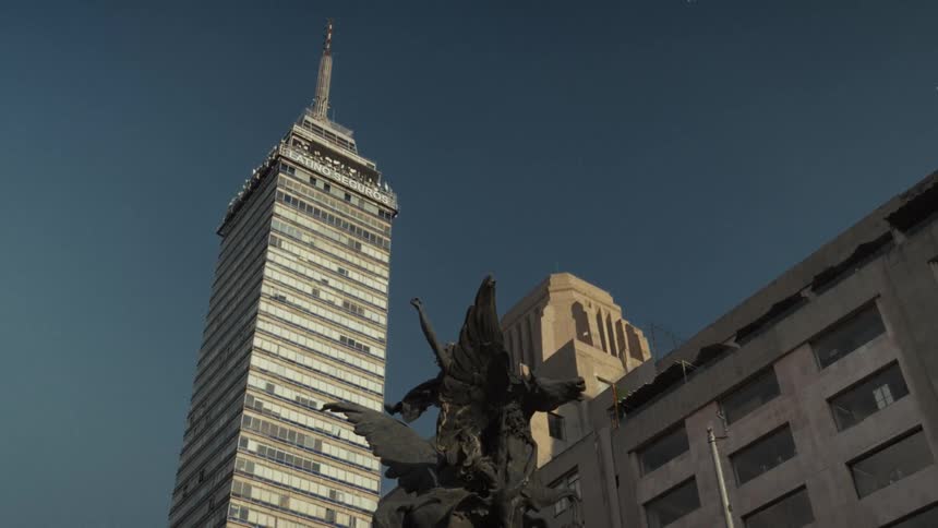 A low-angle shot of the iconic Torre Latinoamericana skyscraper in Mexico City, with a historic statue in the foreground against a clear blue sky