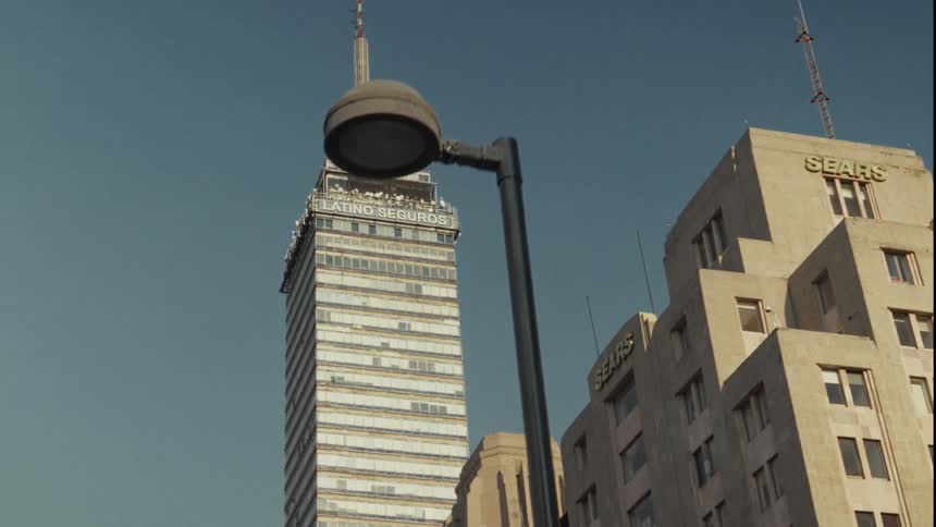 A slow tracking shot from street level reveals the iconic Torre Latinoamericana skyscraper in Mexico City against a clear blue sky