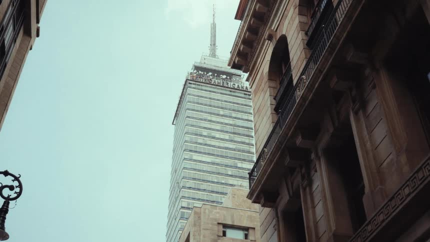 A low-angle view from a city street shows the iconic Torre Latinoamericana skyscraper framed by historic buildings in Mexico City