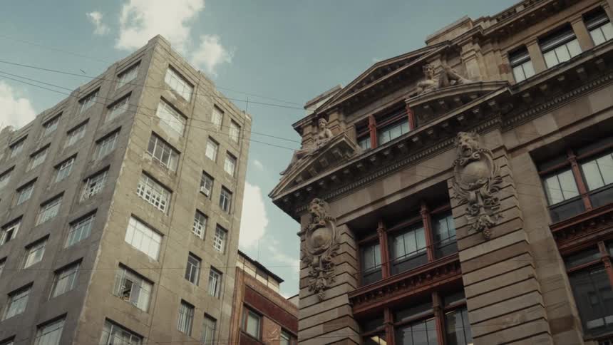 A low-angle view contrasts a weathered, concrete high-rise with an ornate, historic stone building in a city center