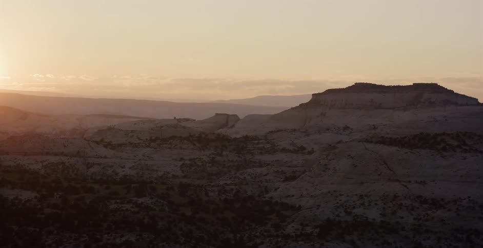Golden hour light bathes a vast desert canyon landscape in warm tones as the sun rises