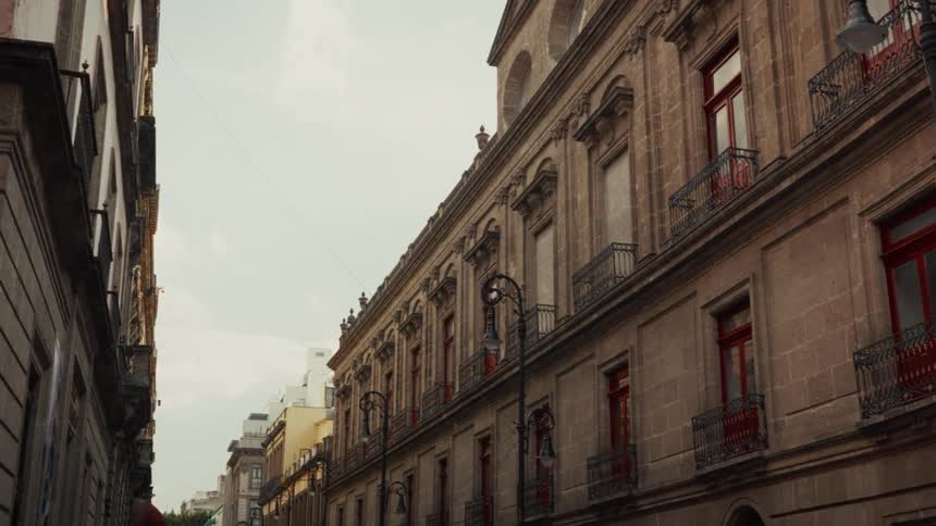 Slow pull back shot of an ornate historic building with red windows on a narrow city street