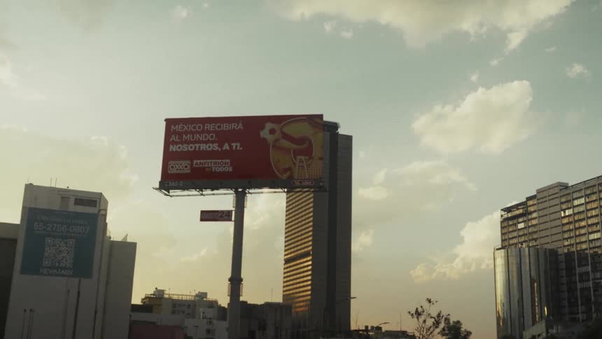 Slow motion driving shot past a large billboard with a skyscraper in the background during a warm sunset in Mexico City