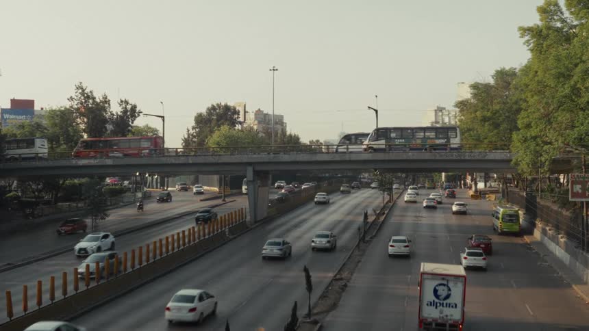 A static wide shot captures the constant flow of traffic on a multi-lane highway and an overpass in a bustling city during the day