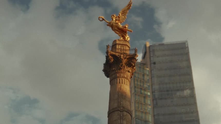The iconic golden Angel of Independence monument stands tall against a modern skyscraper and a cloudy sky in Mexico City