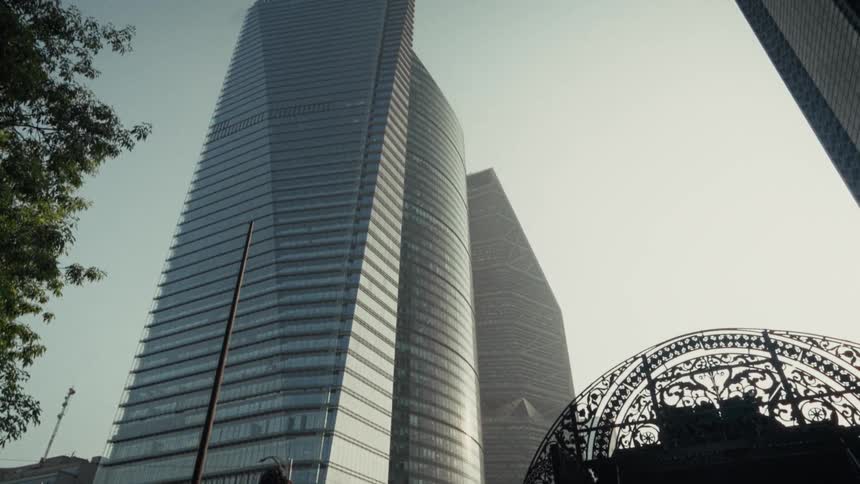 An upward tilt from the ornate Puerta de los Leones reveals the modern skyscrapers of Mexico City's financial district on a hazy day