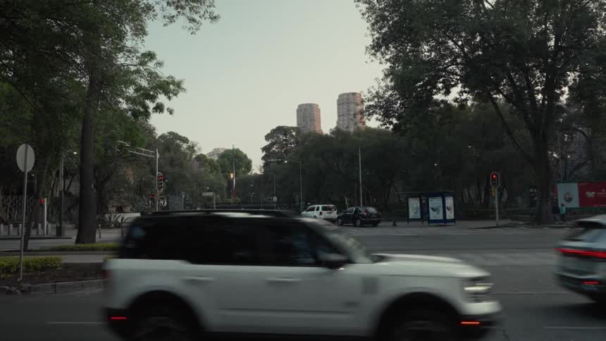 Two police officers stand on a corner as traffic flows by on a city street, with distinctive twin towers rising above the trees in the background
