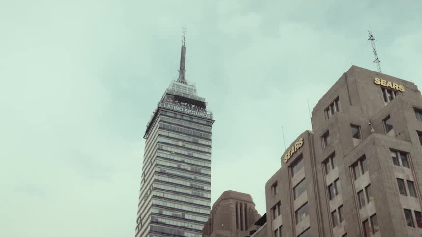 The iconic Torre Latinoamericana stands tall next to a vintage Sears building under an overcast sky in Mexico City