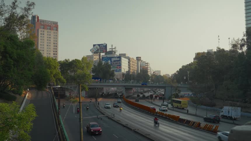 Traffic flows along a busy multi-lane highway and under an overpass in a bustling city during a hazy morning