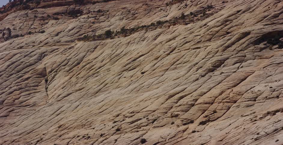 A slow aerial tracking shot reveals the vast, textured patterns of a massive sandstone rock formation in a desert landscape