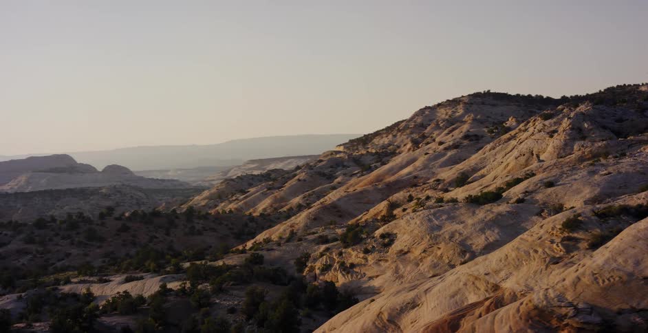 Driving point-of-view shot passing majestic, rolling sandstone hills of a vast desert landscape at sunrise