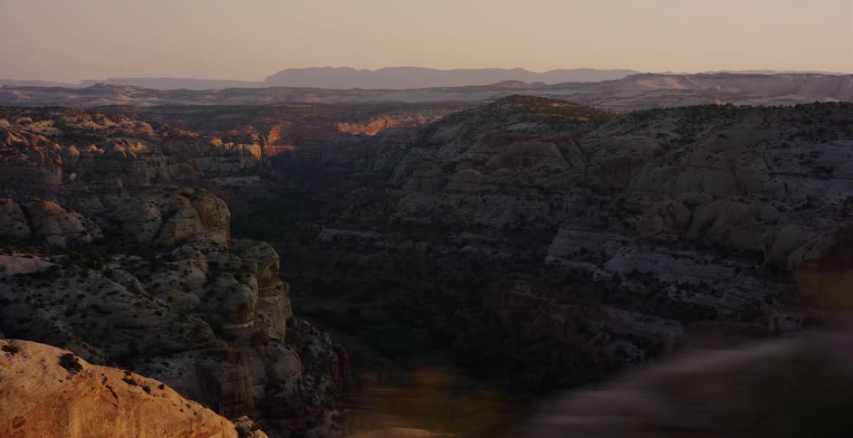 A sweeping aerial pull-back shot reveals a vast desert canyon with rocky formations glowing in the golden hour light