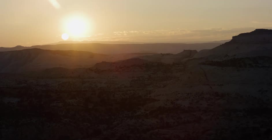 A serene sunrise casts a warm golden glow over a vast and rugged desert canyon landscape