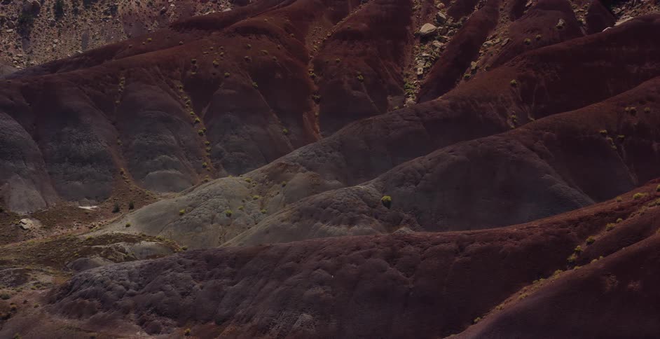 Sunlight illuminates the textured red and brown hills of an arid desert landscape as the camera slowly pulls back to reveal the vastness of the terrain