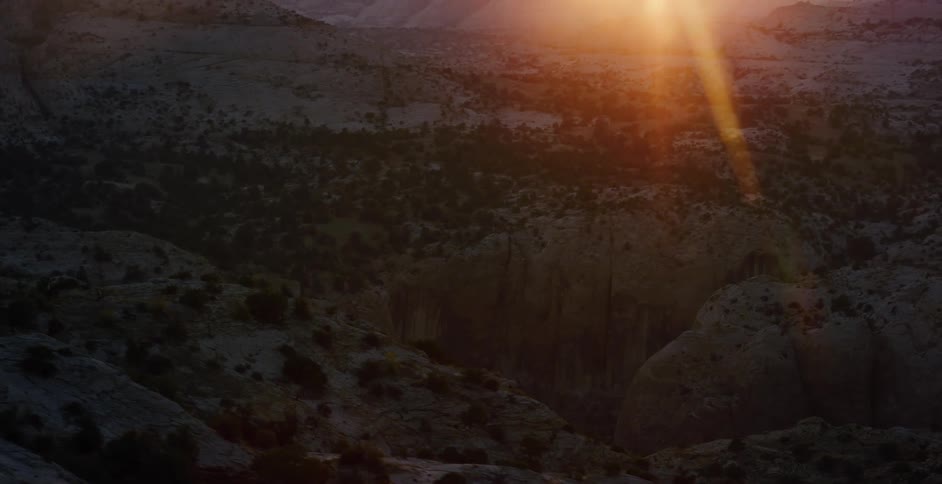 A dramatic zoom out reveals a spectacular sunrise over a vast and rugged desert canyon landscape