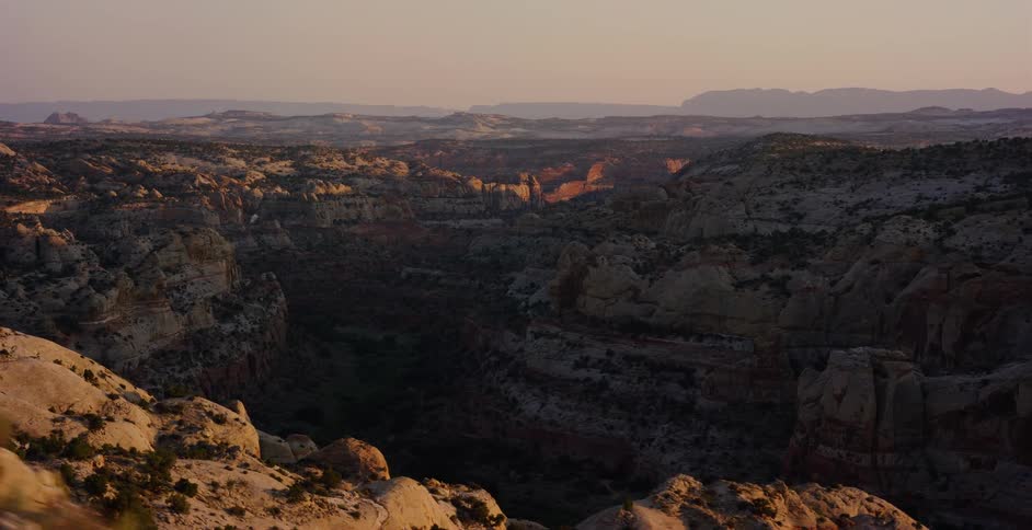 A cinematic tracking shot reveals a vast and rugged desert canyon landscape bathed in the warm, golden light of sunset