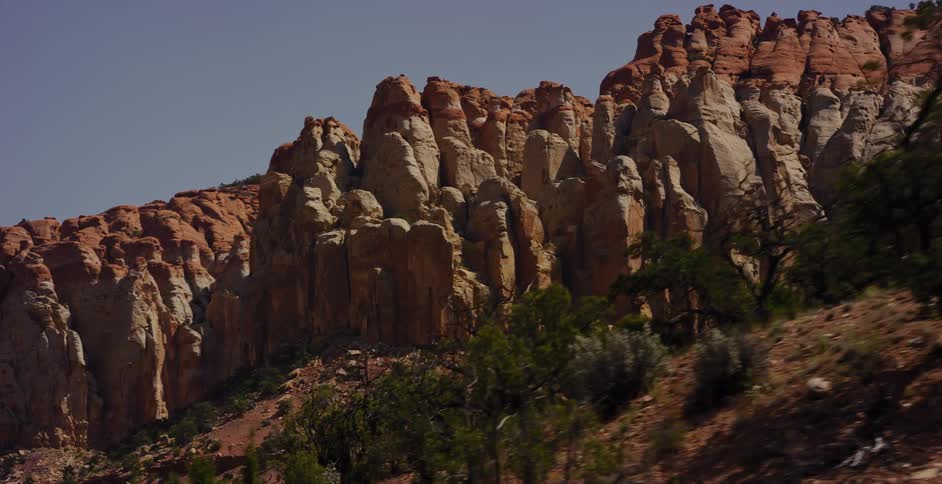 A slow-motion tracking shot reveals the majestic and weathered red rock cliffs of a desert landscape under a clear sky