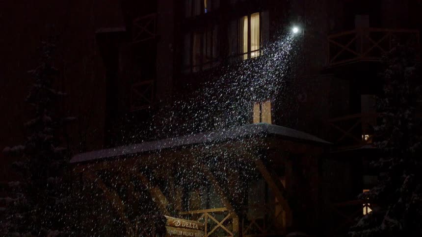 Light on side of building illuminating the snow as it falls at night