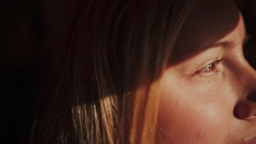 Close up of a woman's eye as a ray of warm sunlight gradually moves across her face