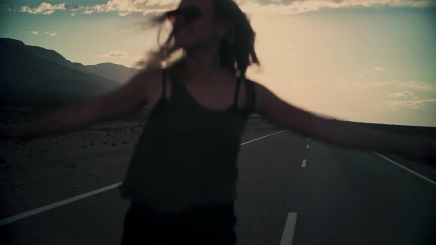 A free-spirited woman joyfully spins in slow motion on an empty desert road at sunset