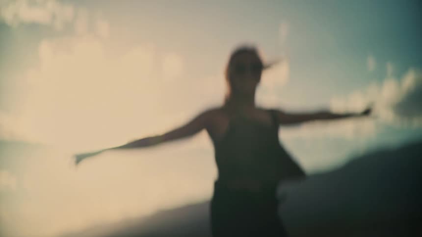 Dreamy slow motion shot of a joyful woman dancing and twirling against a sun-drenched sky