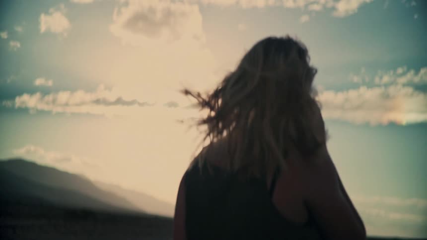 Slow motion of a carefree woman with sunglasses smiling as the wind blows through her hair at sunset