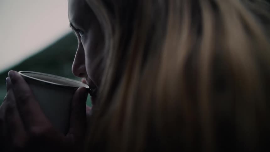 Slow motion close-up of a thoughtful woman drinking a warm beverage from a mug in a moody outdoor setting