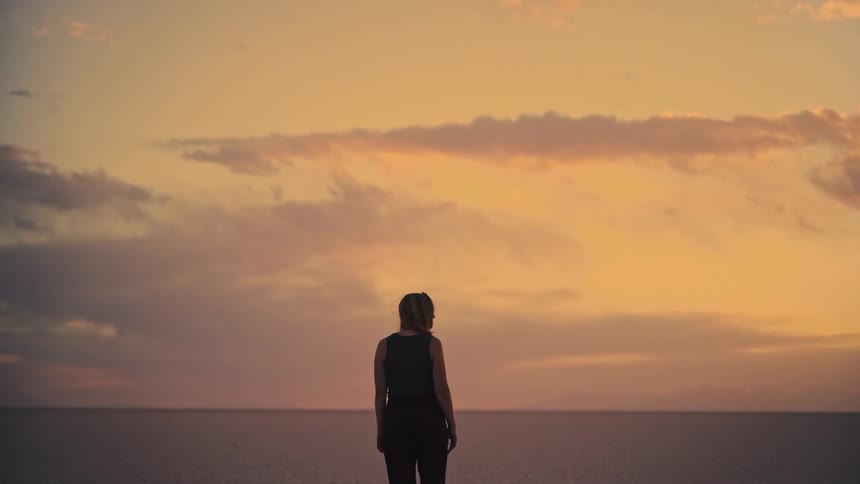 A lone woman stands in a vast, empty landscape, watching the beautiful colors of a sunset sky