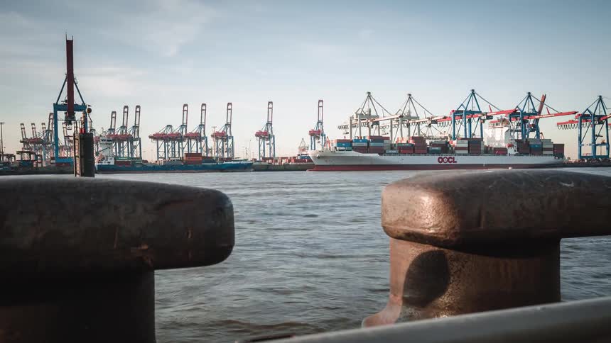 A dynamic timelapse captures the bustling activity of cargo ships and ferries in an industrial port, viewed from behind a rusty bollard