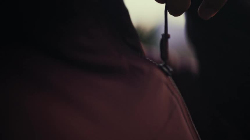 A close-up slow-motion shot shows a young woman zipping up her outdoor jacket to her chin