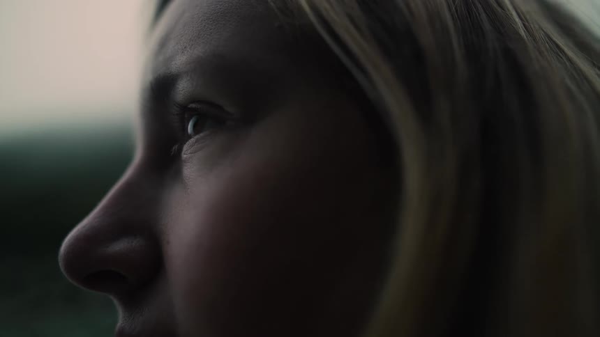 A moody, silhouetted close-up of a young woman's face in profile as she gazes intently