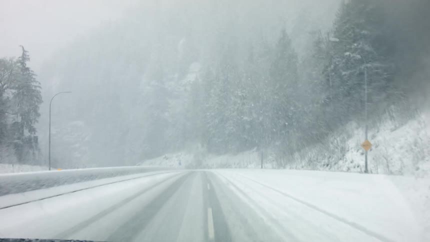 A car uses its wipers as it is driven on a snowy road