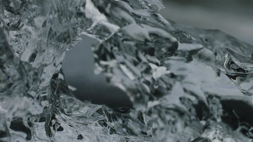 A macro close-up shot of a transparent glacier ice chunk with the blurred ocean in the background at Diamond Beach, Iceland
