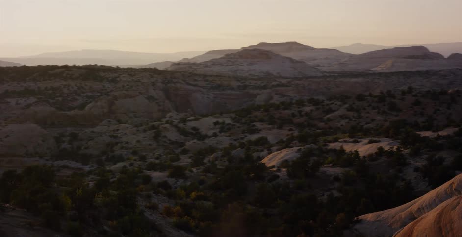 A scenic tracking shot reveals the vast, rocky terrain of a desert canyon landscape during a beautiful golden hour