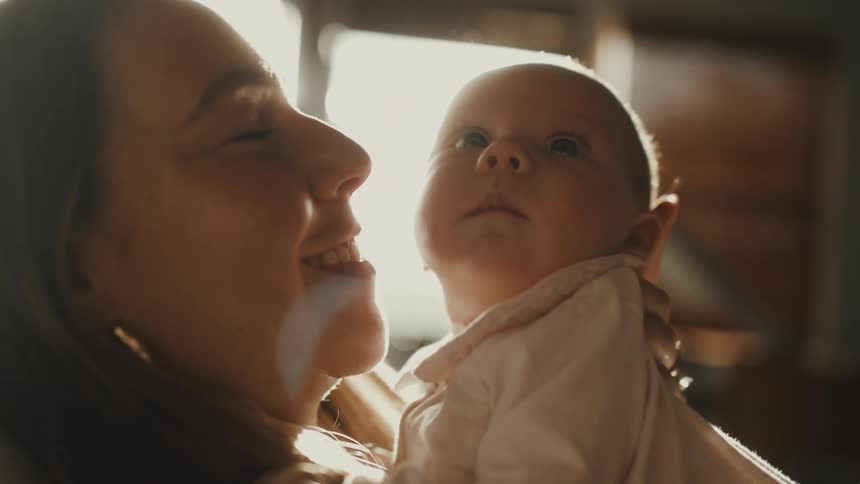 A tender moment between a mother and her newborn as she holds and kisses the baby in soft, golden light