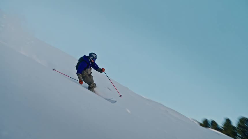 A skier skillfully carves through fresh powder down a steep mountain face in a breathtaking slow-motion sequence