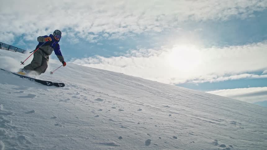An expert skier gracefully descends a steep, snowy mountain, kicking up a huge cloud of fresh powder in super slow motion