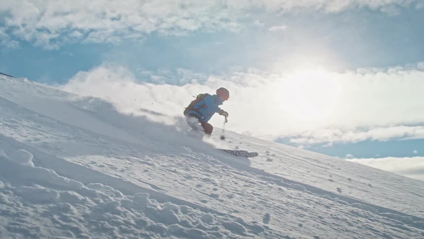 A professional skier carves down a powdery mountain slope in super slow motion on a beautiful sunny day