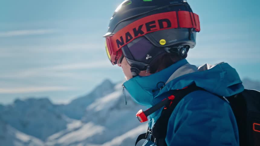 Slow motion close-up of a skier putting on goggles and looking out at the vast snowy mountain range