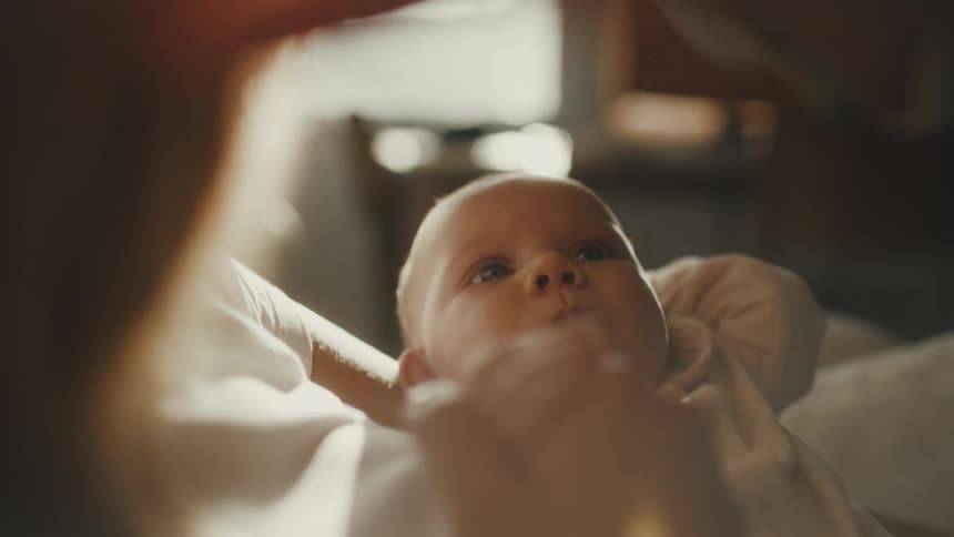 An intimate over-the-shoulder close-up of a newborn baby gazing up at its mother as she gently touches its face