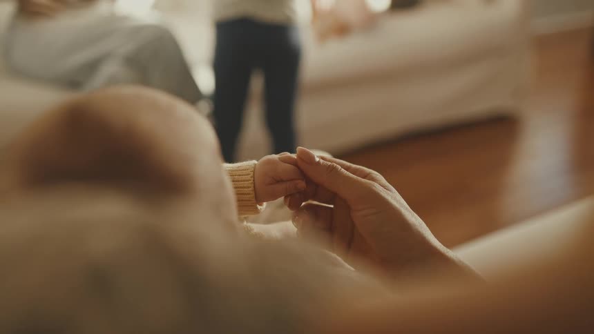 A tender moment as a newborn baby's tiny hand grips its mother's finger in a cozy living room