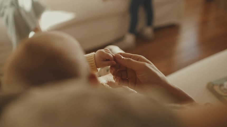 A mother gently holds her newborn baby's tiny hand in a tender and loving close-up shot at home