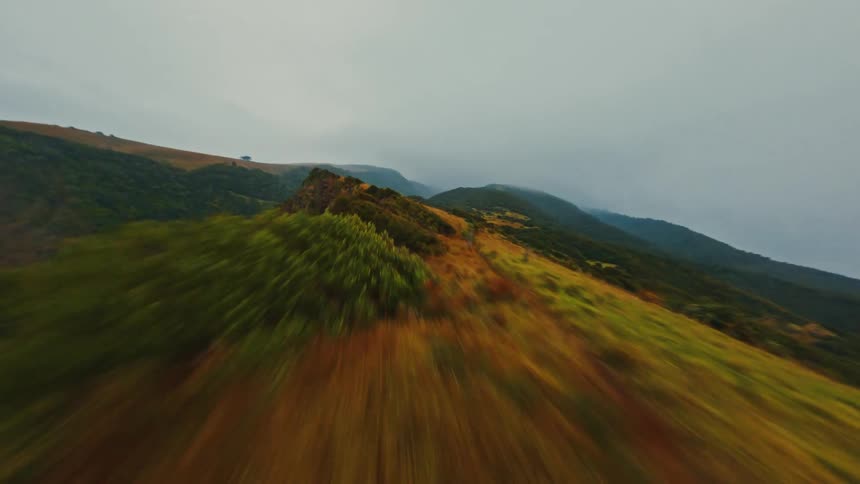 An exhilarating FPV drone flight speeds along a vibrant, grassy mountain ridge under a moody, overcast sky
