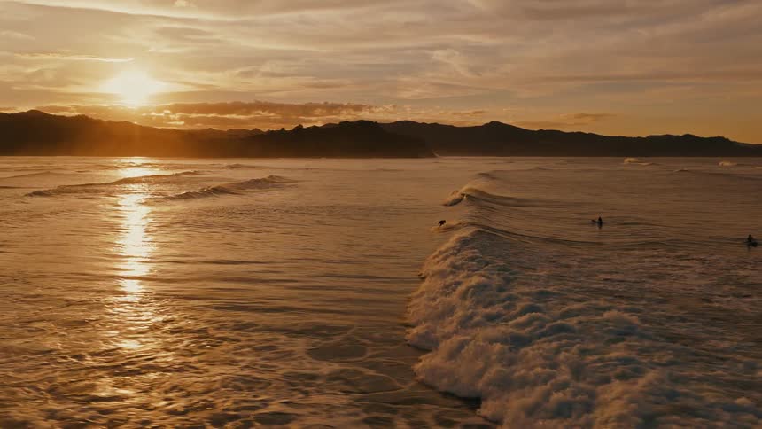 Cinematic slow motion aerial of a surfer riding a perfect wave during a golden sunset over the ocean