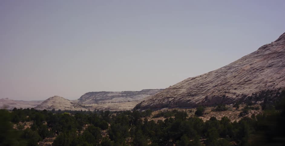 A scenic drive through a desert canyon reveals vast, sloping rock formations and green scrubland