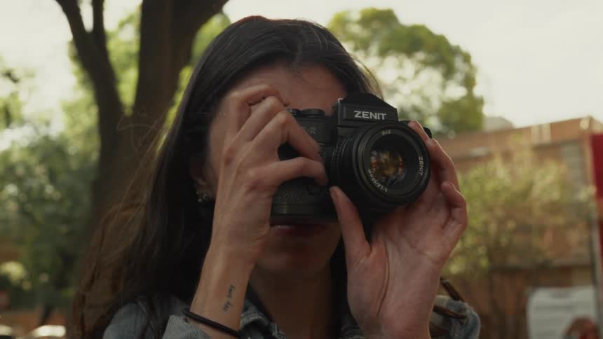 A female photographer with long dark hair focuses her vintage film camera to take a picture outdoors